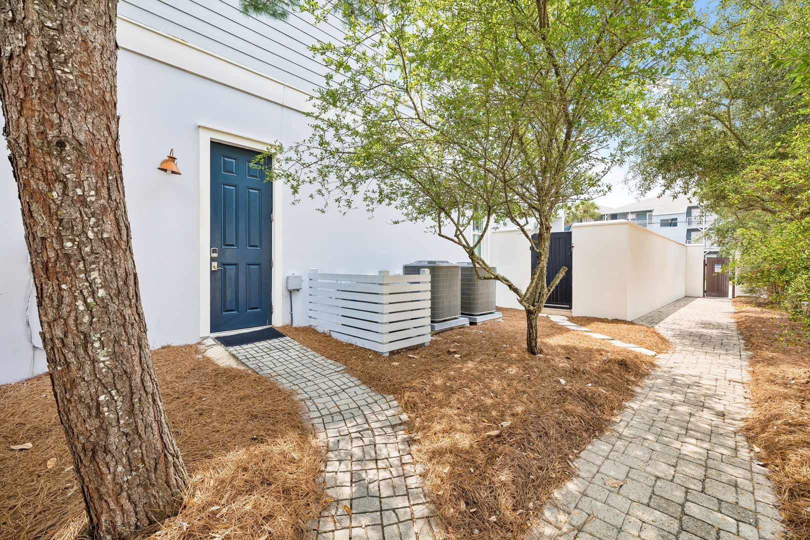 A charming blue front door welcomes guests along a winding cobblestone path, framed by natural landscaping and shaded by mature trees for a peaceful arrival.