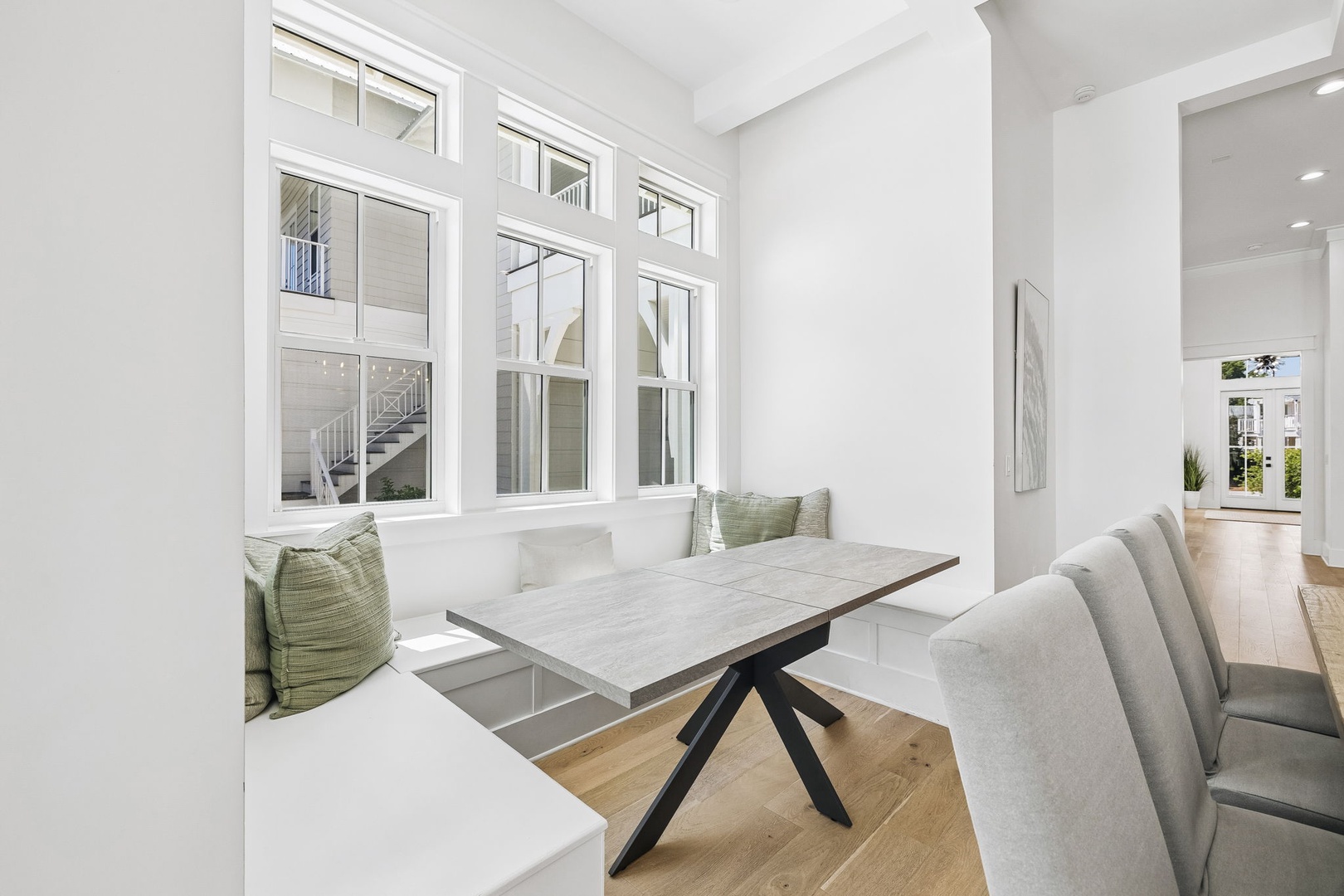 Gather around a modern dining table framed by bright windows, where built-in bench seating and soft cushions create your cozy breakfast nook. Open, airy, and bathed in natural light—your mornings start here.