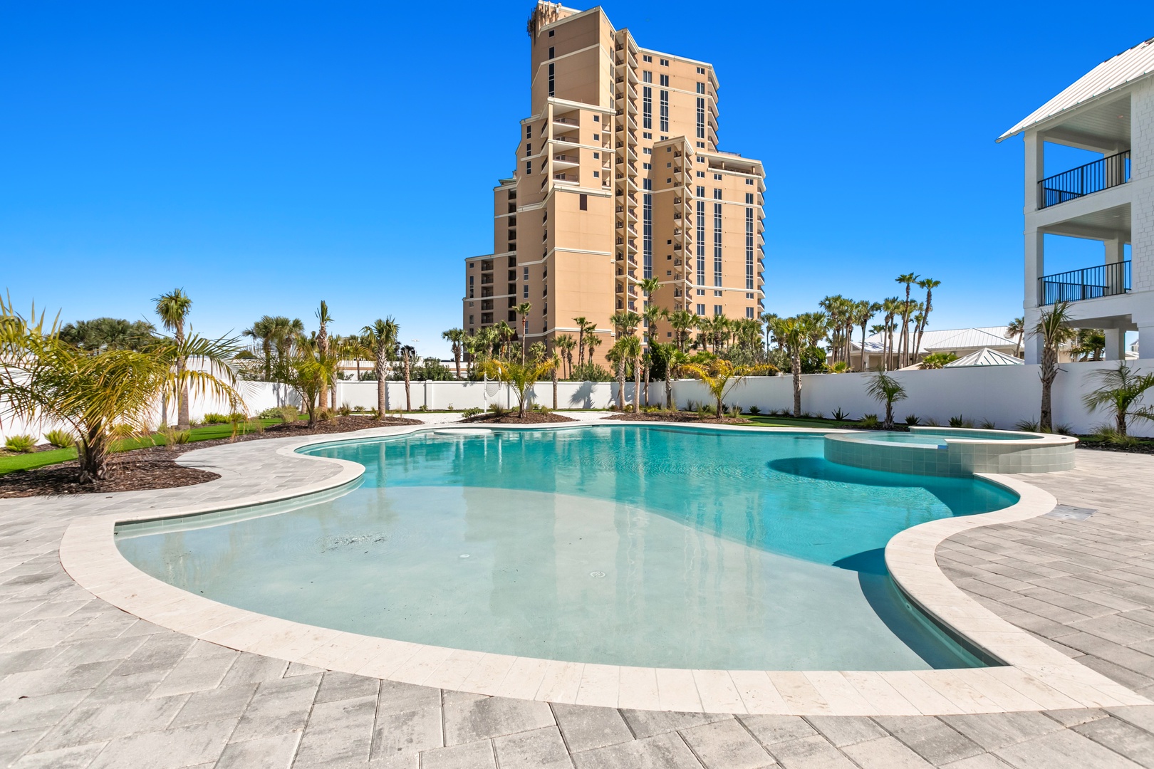 A resort-style pool with a wading area and tropical palms creating your perfect backdrop for Florida getaways. Sunny skies and modern architecture frame your outdoor oasis.
