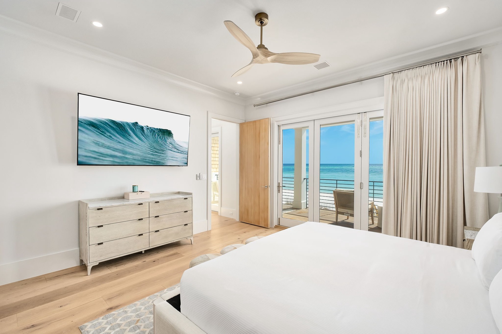 Wake up to stunning ocean views from your private balcony in this serene bedroom featuring crisp linens and coastal charm.