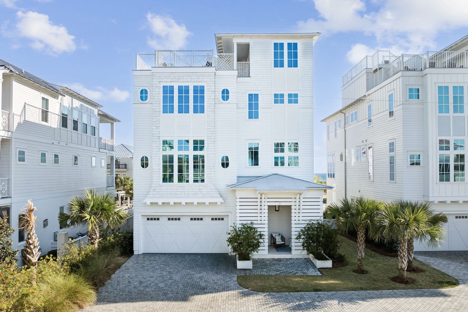 Modern coastal property featuring white exterior with balconies and palm-lined entrance in sunny residential community.