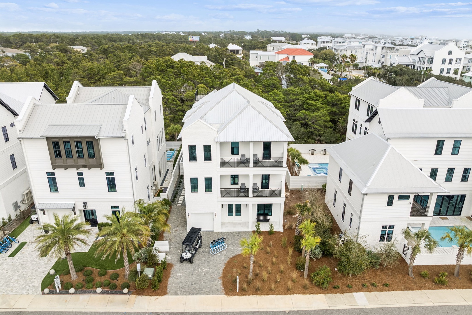 Aerial view of a modern white vacation home nestled in a tropical coastal neighborhood with lush greenery and nearby beaches.