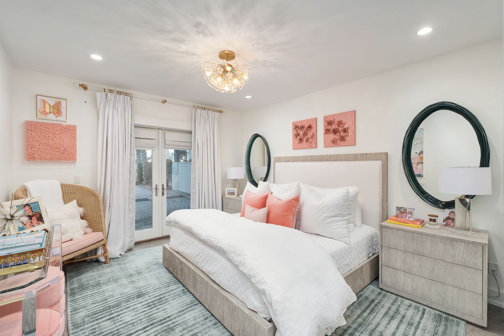 Sink into plush bedding under a sparkling chandelier in your serene retreat, where coral accents and peaceful hues help you unwind after a day exploring.
