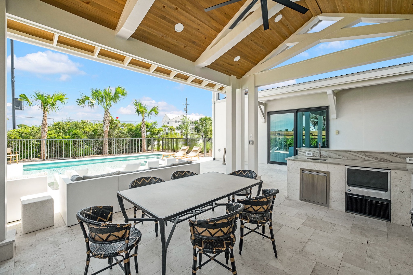 Your covered outdoor dining area opens to the pool and lush tropical palms, with a full outdoor kitchen ready for relaxed meals in the Florida sunshine.