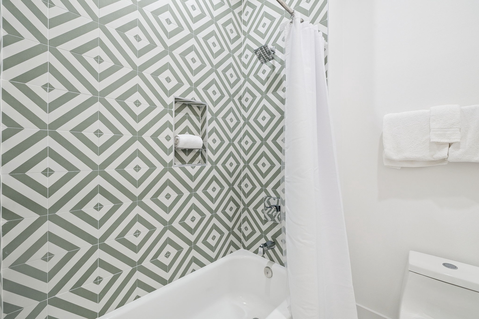 Unwind in your stylish bathroom featuring geometric tiles and a relaxing tub-shower combo with fresh white towels.