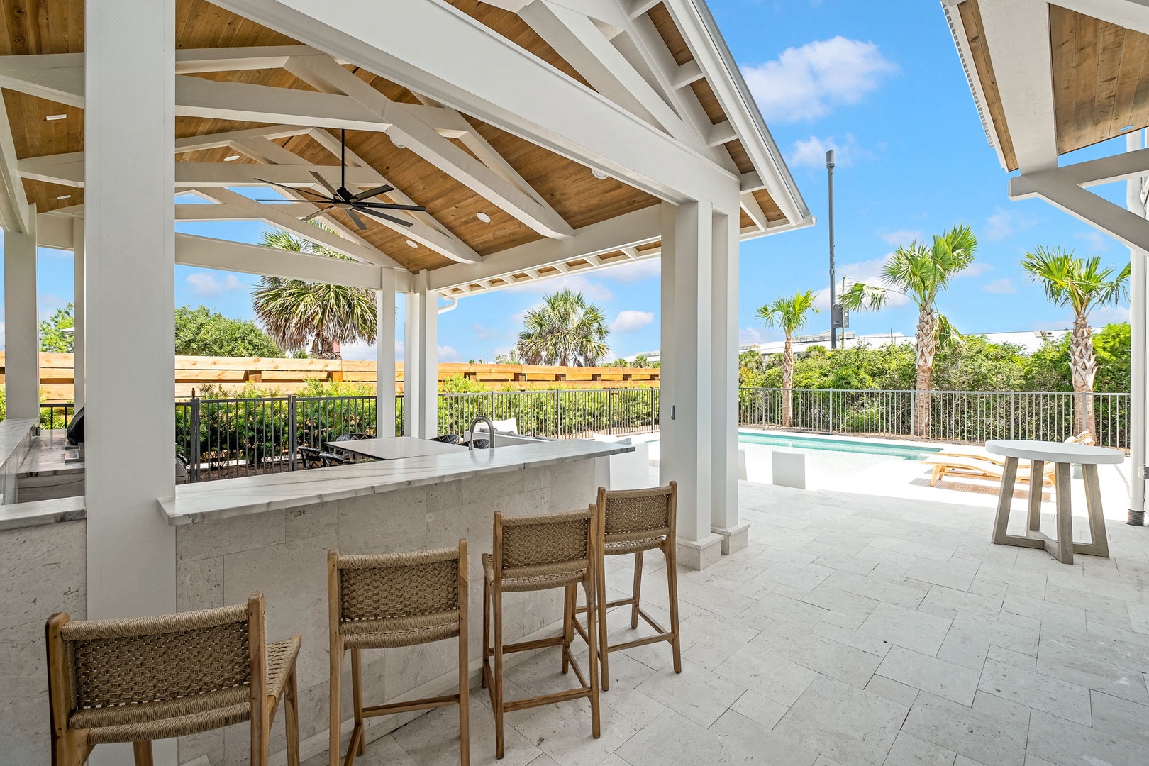 This poolside bar area invites you to gather under beautiful beamed ceilings while gazing out at swaying palms and sunny skies—perfect for serving refreshments as you entertain in style.