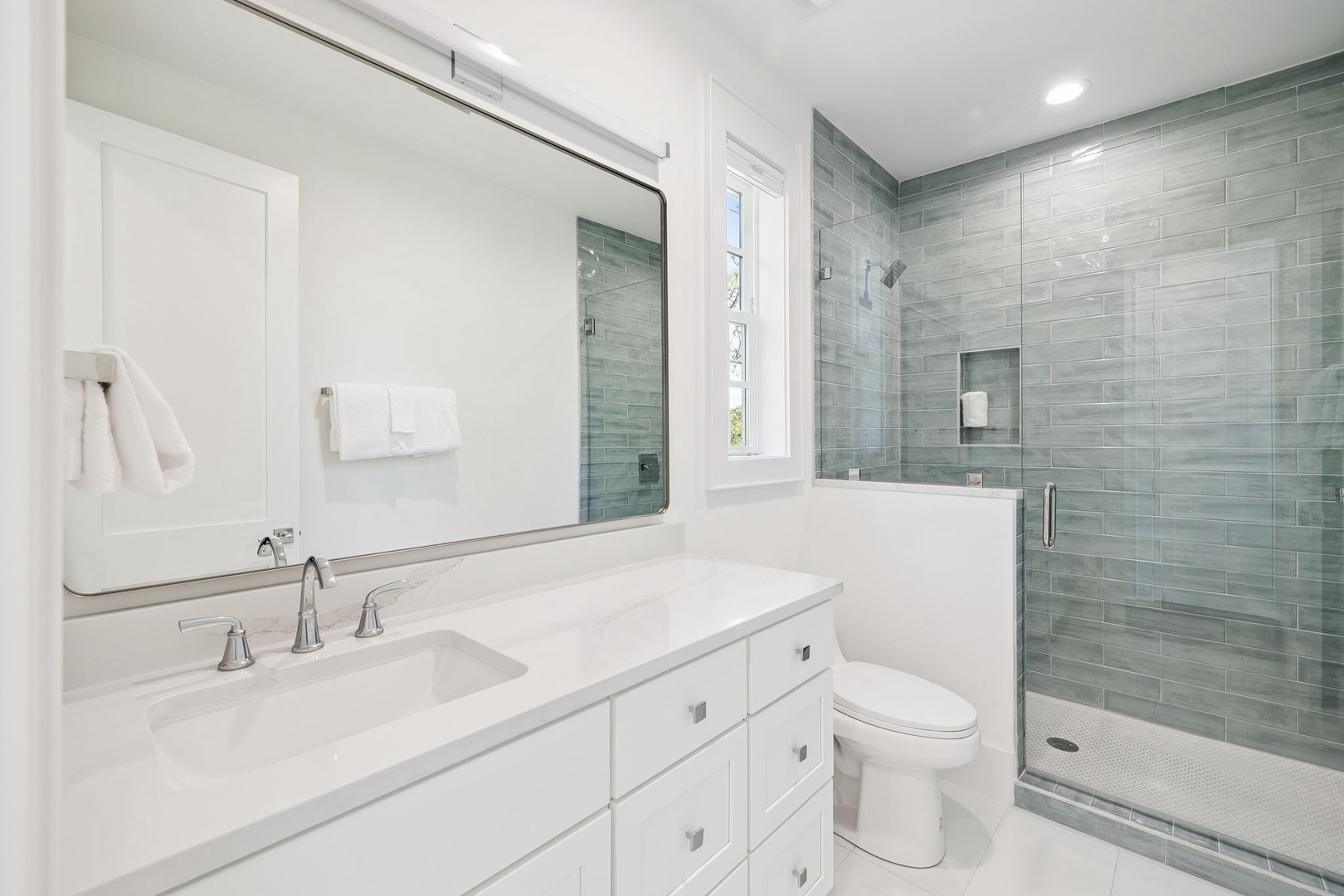 Relax in your spa-inspired bathroom featuring pristine marble countertops, a luxurious glass-enclosed shower, and elegant sage tile work.