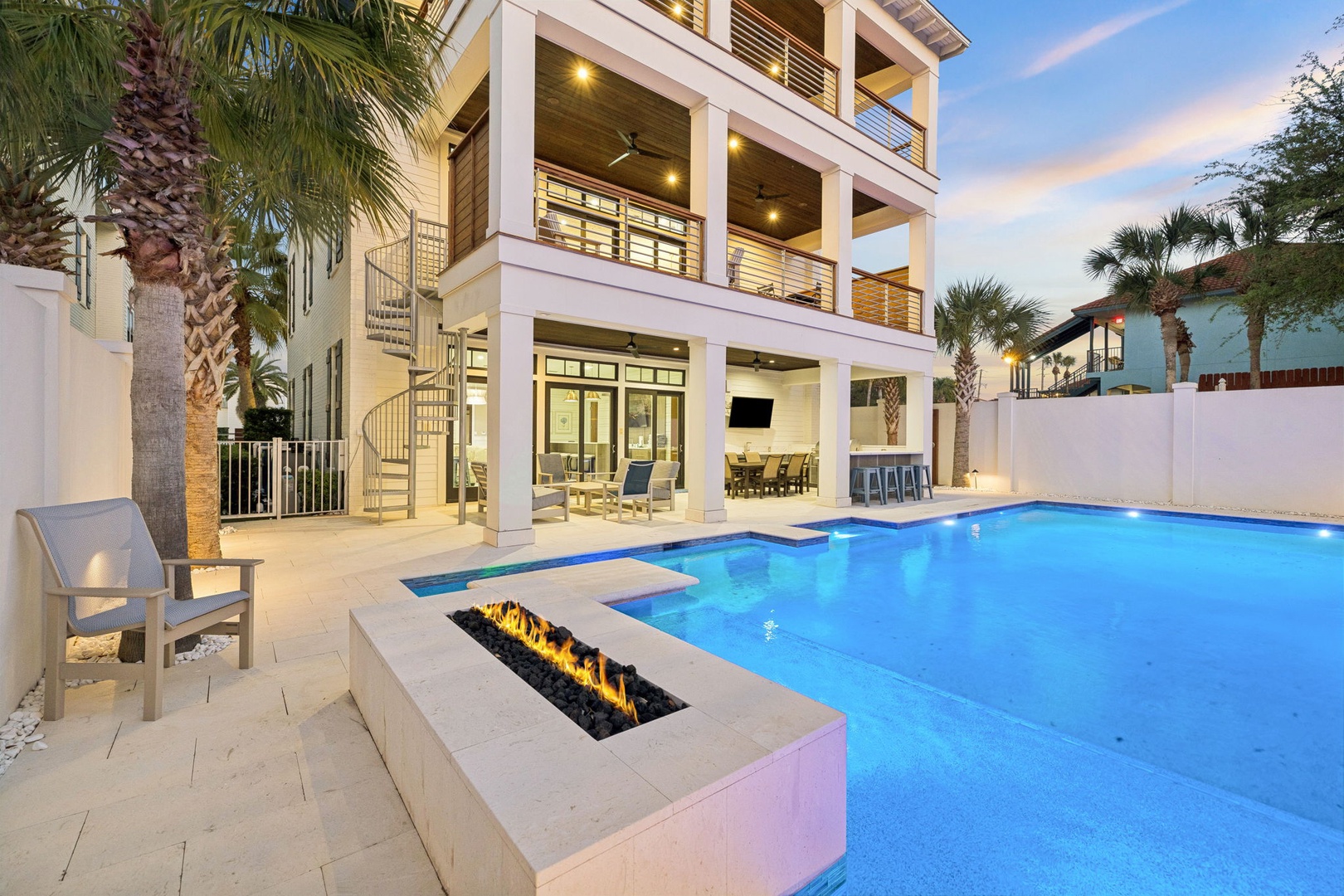 Modern three-story beachside villa with private pool and fire pit, surrounded by tropical palms in an upscale coastal neighborhood.