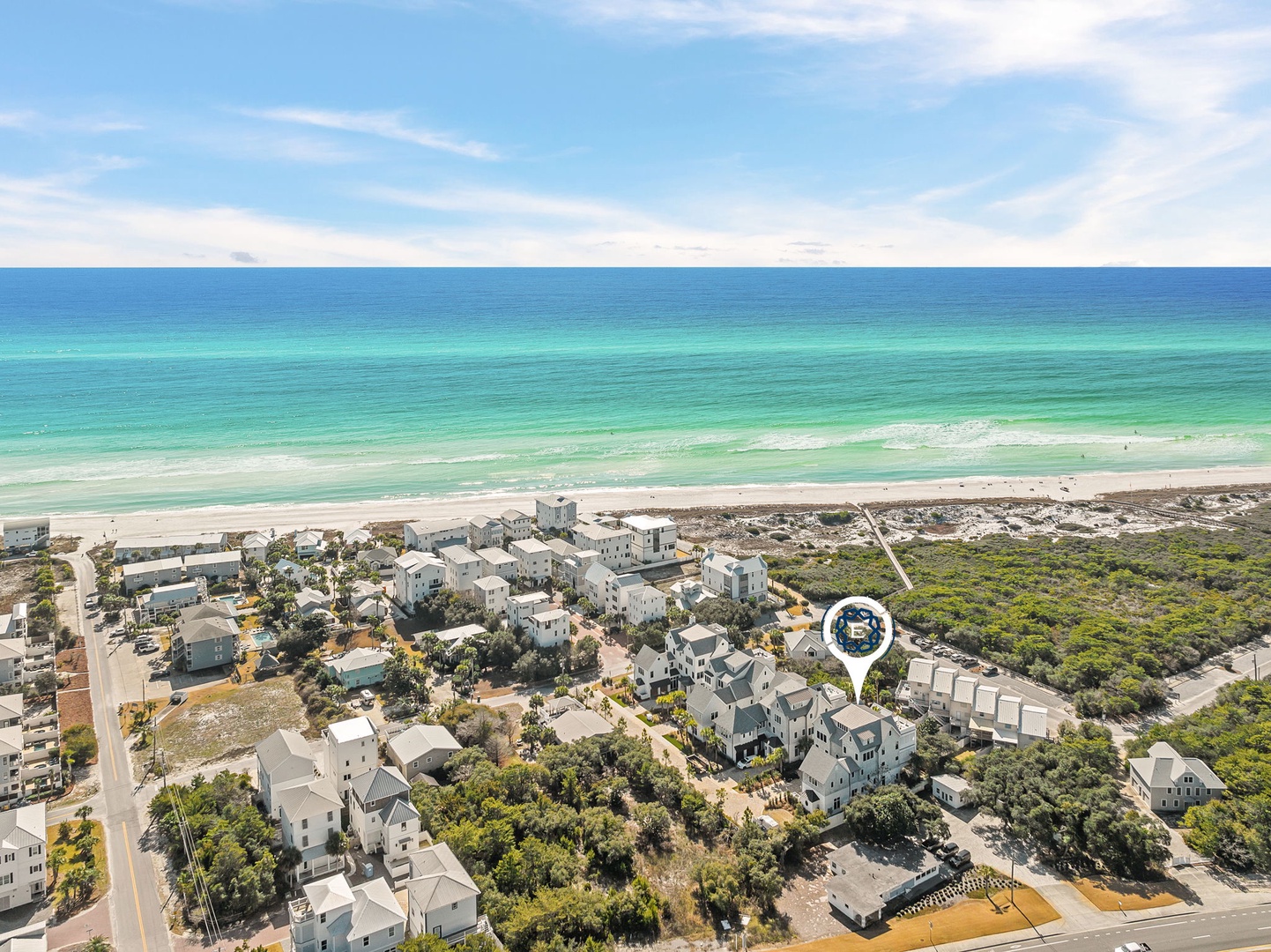 Aerial view of beachfront community with pristine white sand beach and emerald waters stretching to the horizon.