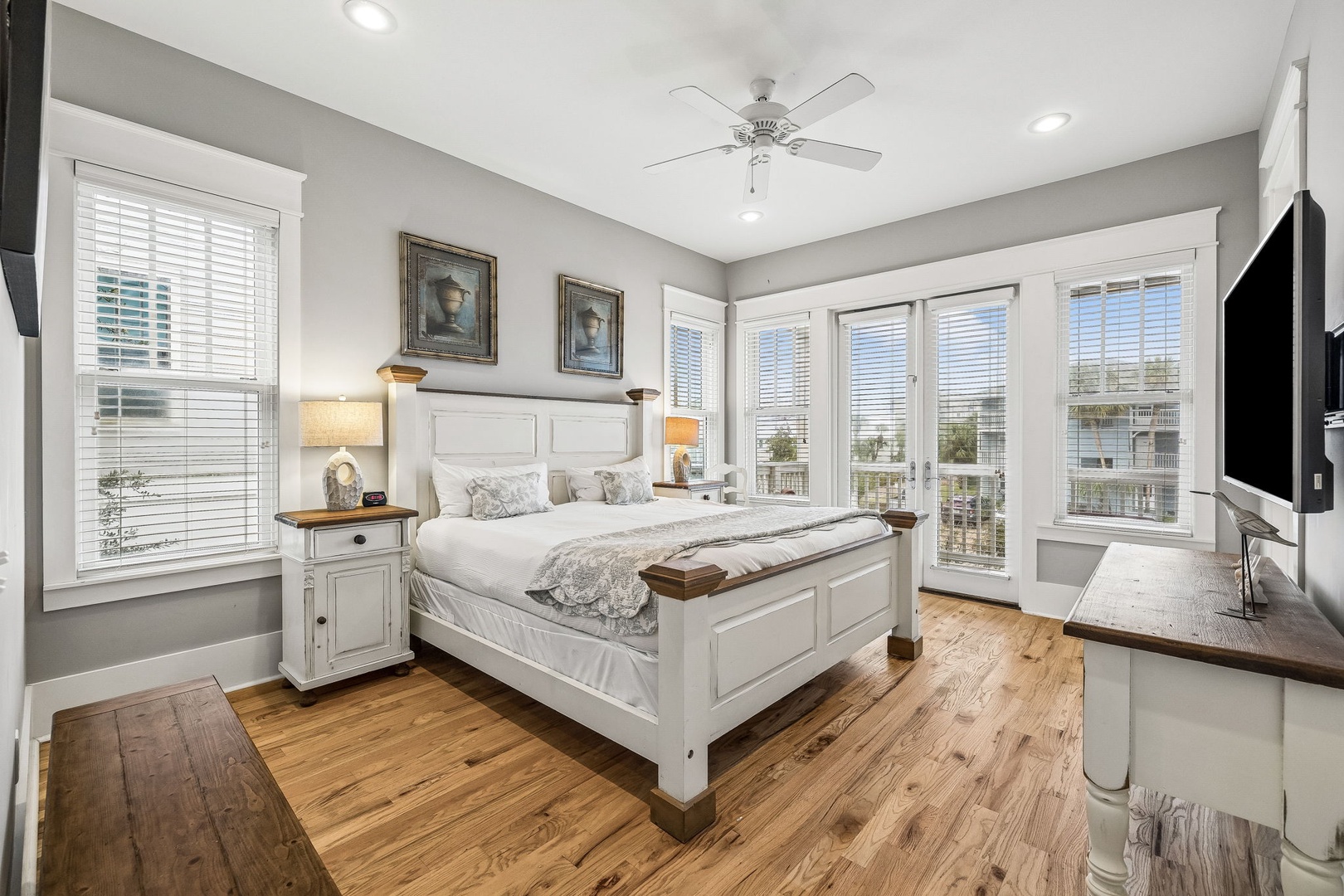 Step into your serene retreat, where soft morning light filters through expansive windows and a plush bed awaits your arrival. Feel the gentle breeze from the ceiling fan as you relax in this thoughtfully designed coastal-inspired space.