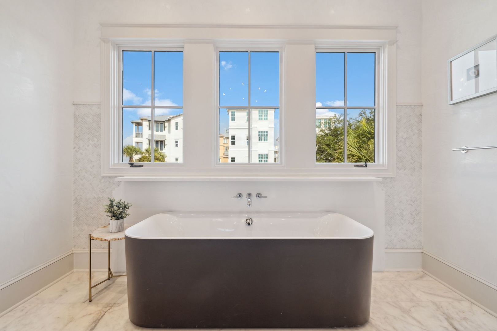 Soak in this elegant freestanding tub, where natural light pours through triple windows and subtle tile work adds a touch of sophistication to your bathing retreat.