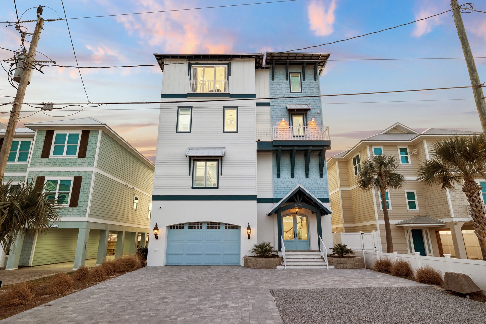 Modern coastal home with three levels and balconies, featuring palm trees and paved driveway in a beachside neighborhood setting.