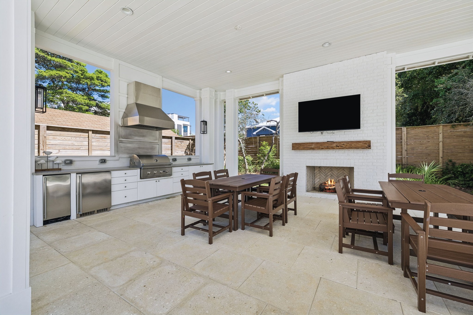 Your covered outdoor entertaining space combines a full kitchen with stainless appliances, cozy fireplace, and multiple dining areas—perfect for gathering day or night with views of the lush garden.