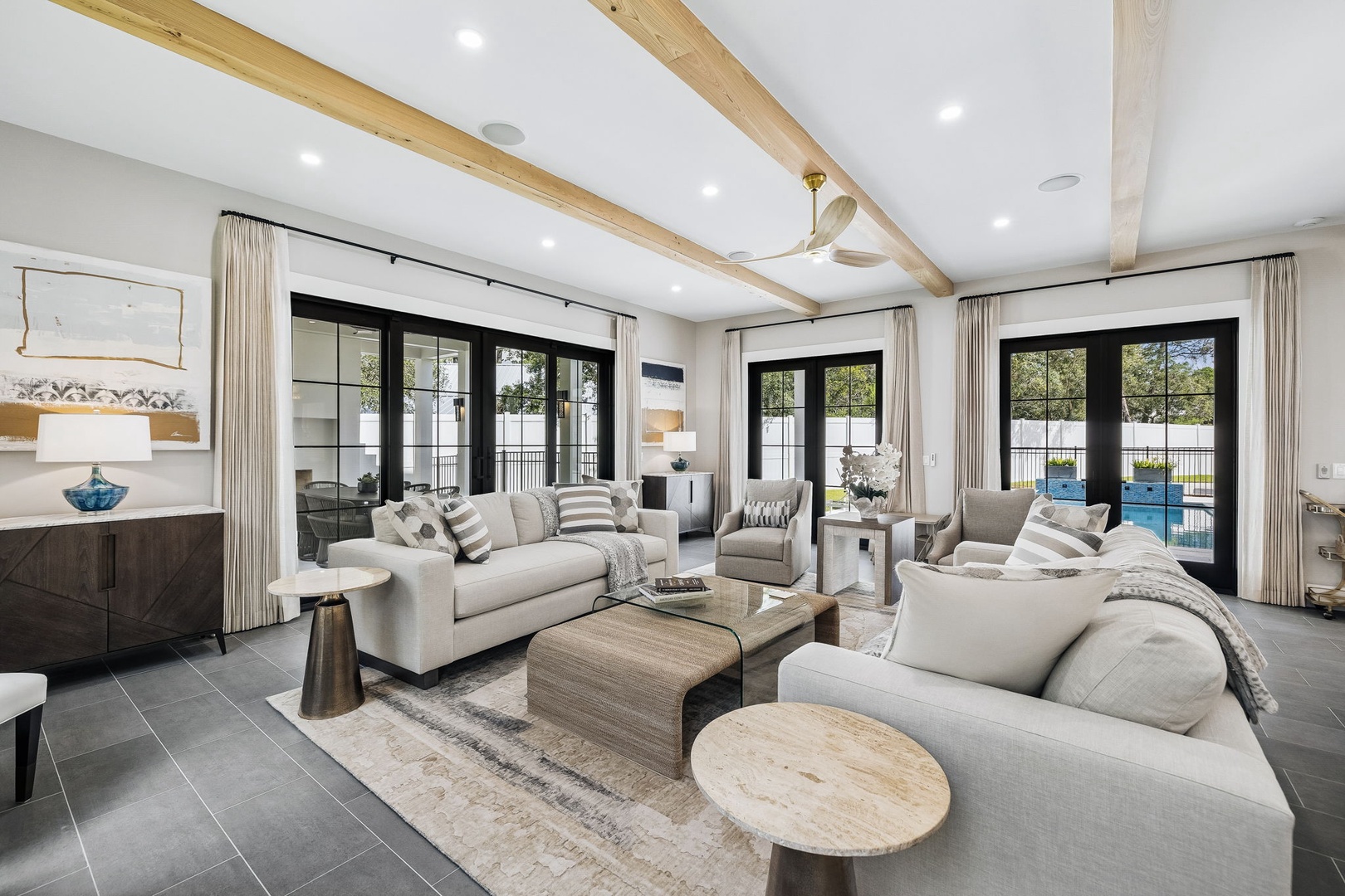 Gather in this light-filled living room where natural wood beams frame soaring ceilings and multiple French doors open to your private pool. Sink into plush seating and let the view draw you outside to endless sunny days.