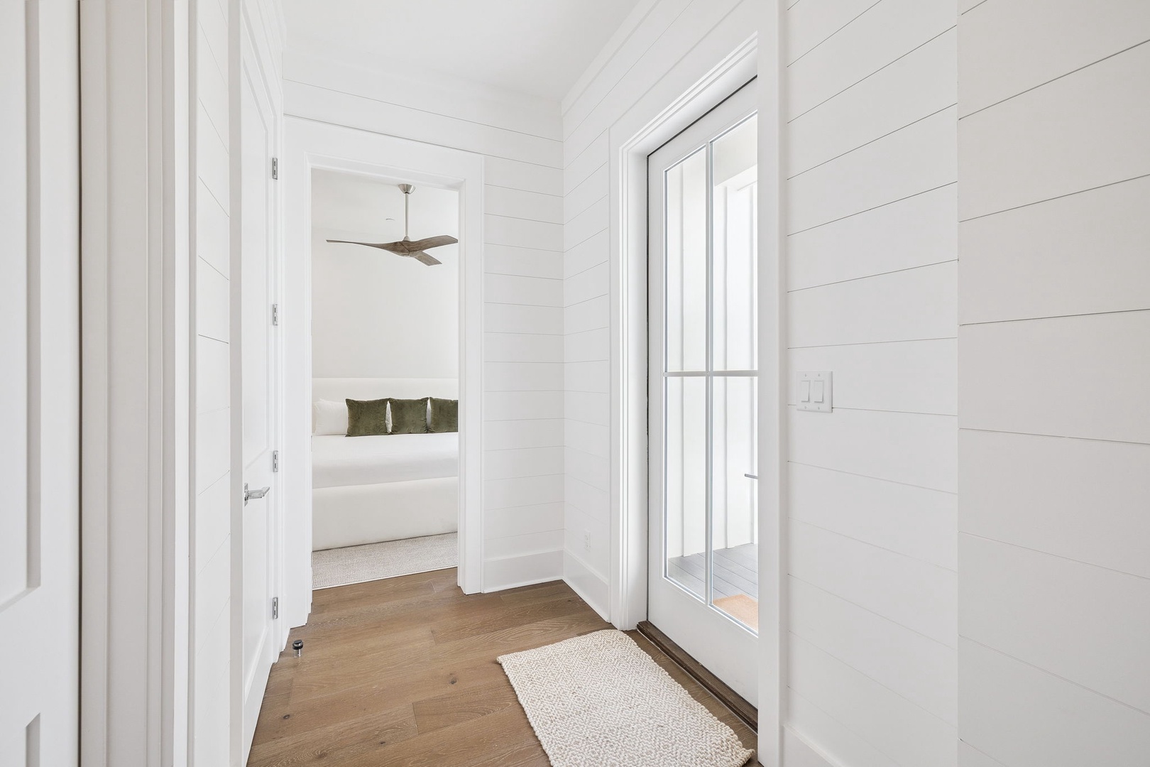 Step into your bright hallway where clean white shiplap walls and warm hardwood floors guide you to your peaceful bedroom retreat.