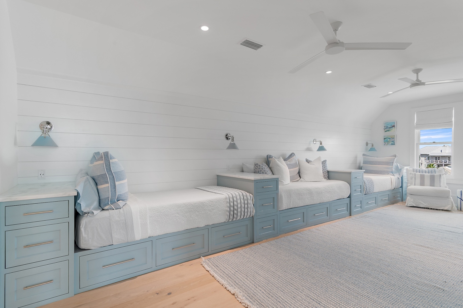 Relax in this bright coastal bedroom where crisp white shiplap walls meet soft blue built-in beds with under-bed storage. Reading lights and ceiling fans keep you comfortable as you unwind.