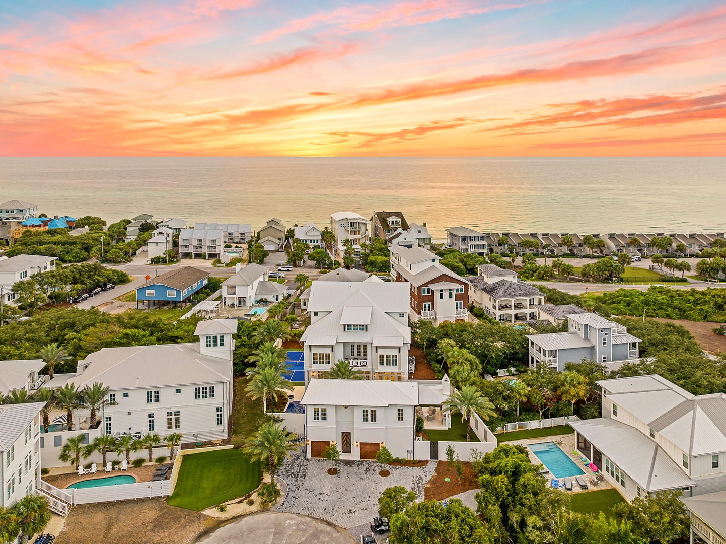 A stunning coastal community captured at sunset, with charming beach homes nestled among palm trees just steps from the shoreline.
