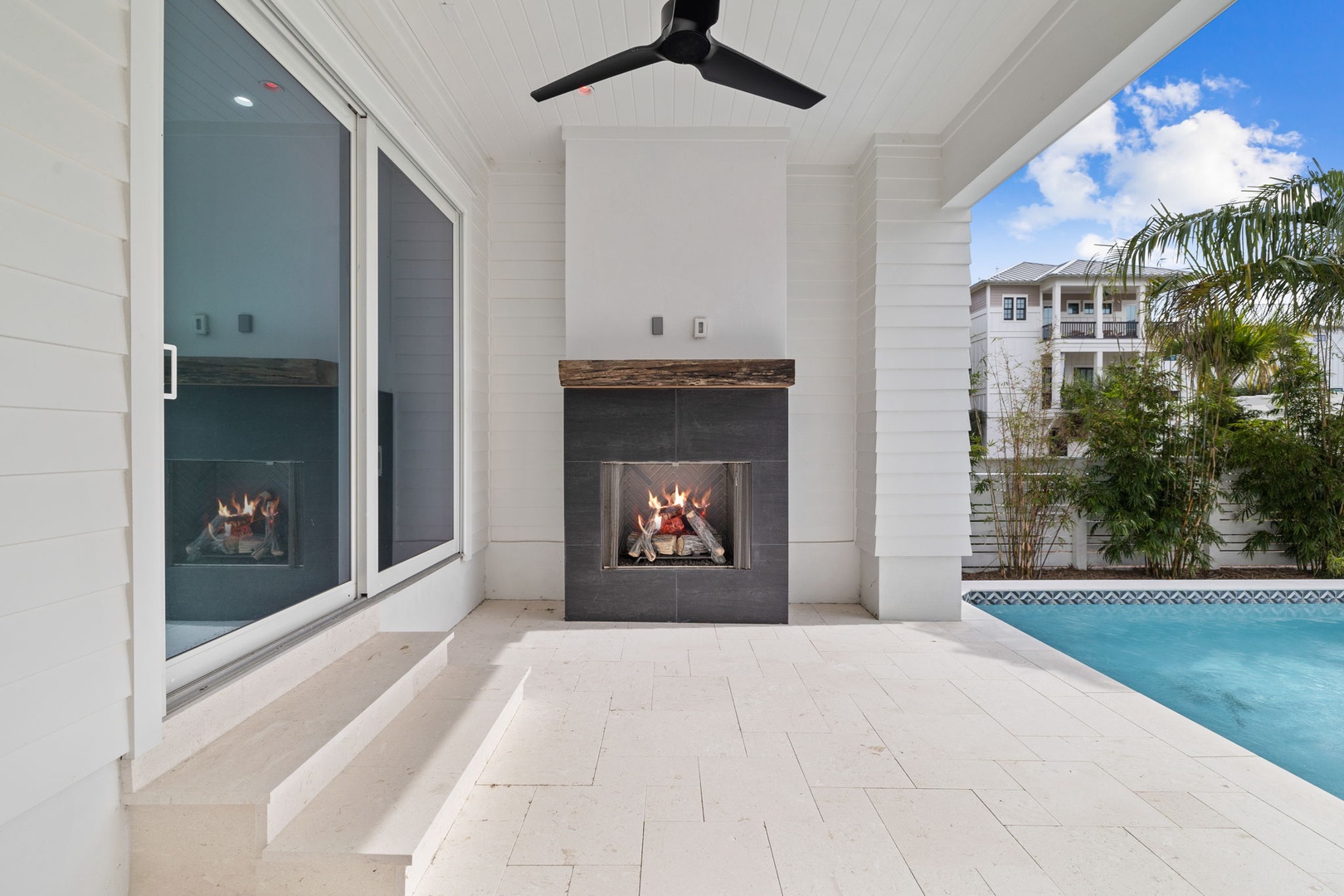 Relax by your crackling fireplace on this elegant covered terrace, where cooling ceiling fans and pool views create the perfect evening retreat.