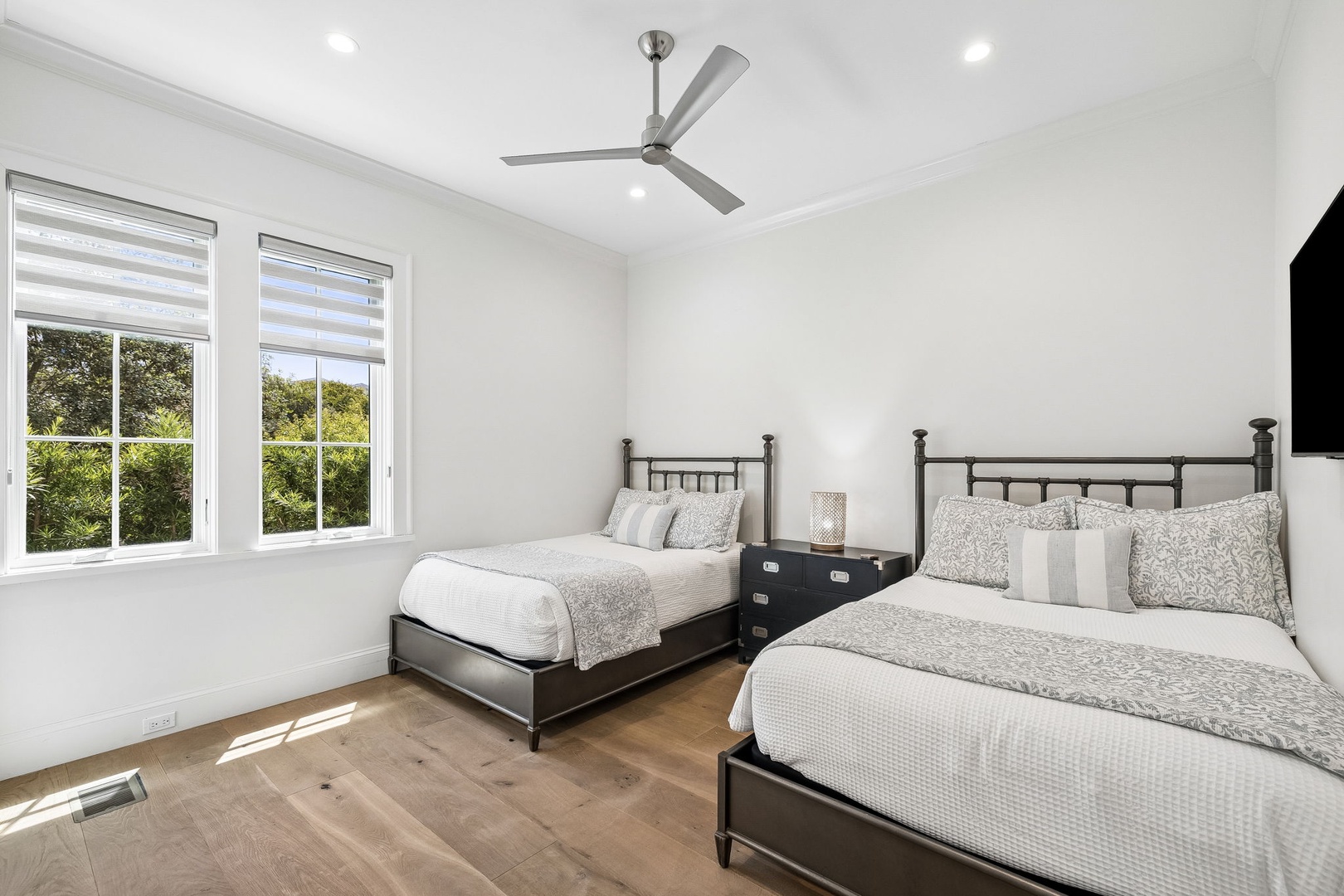 Your bright guest room offers two comfortable beds with soft linens, a ceiling fan for cooling comfort, and windows framing peaceful garden views—ideal for restful mornings.