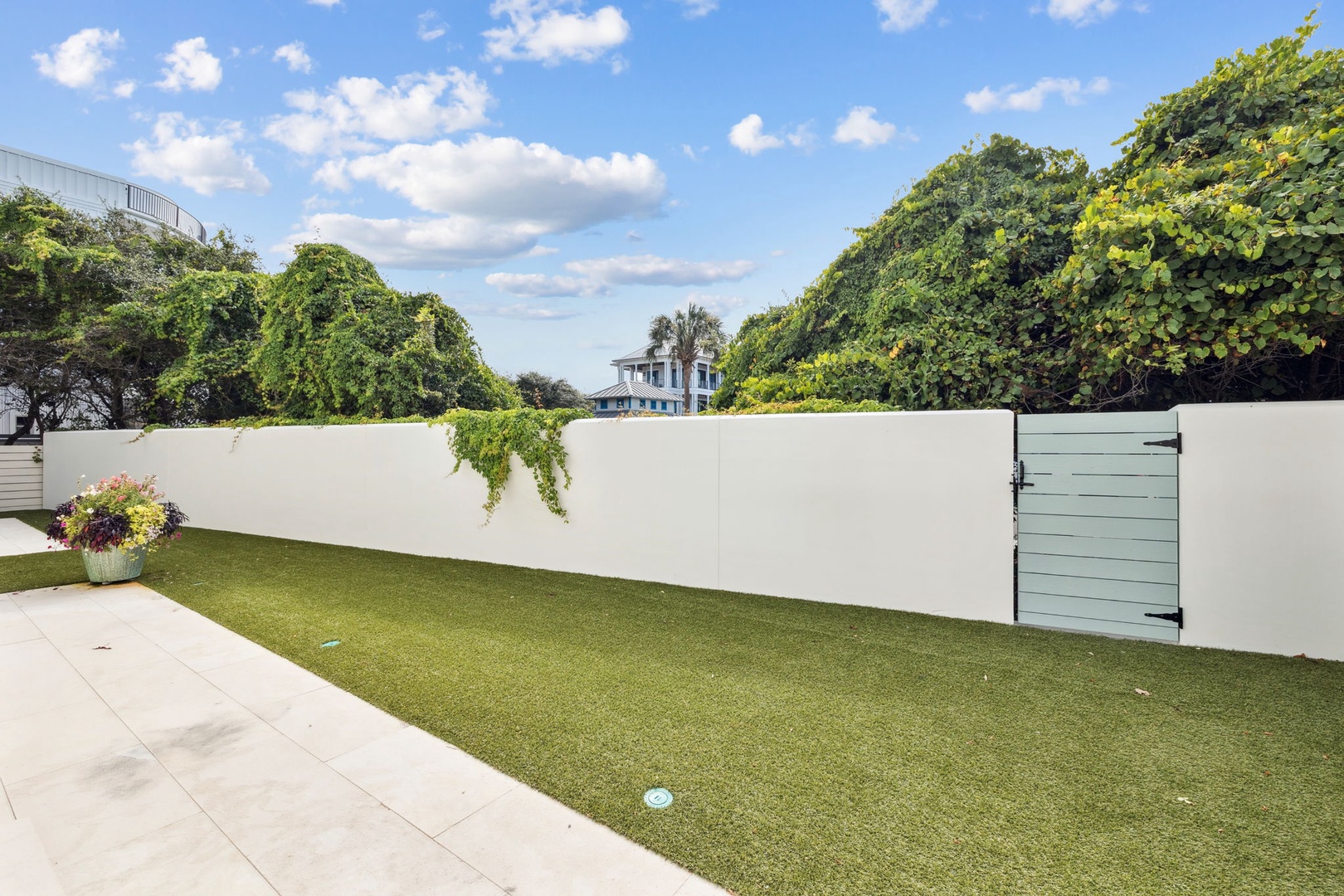 Step outside to your private grassy courtyard, enclosed by white walls and lush green foliage—a peaceful spot where you can relax under blue skies and enjoy quiet moments outdoors.