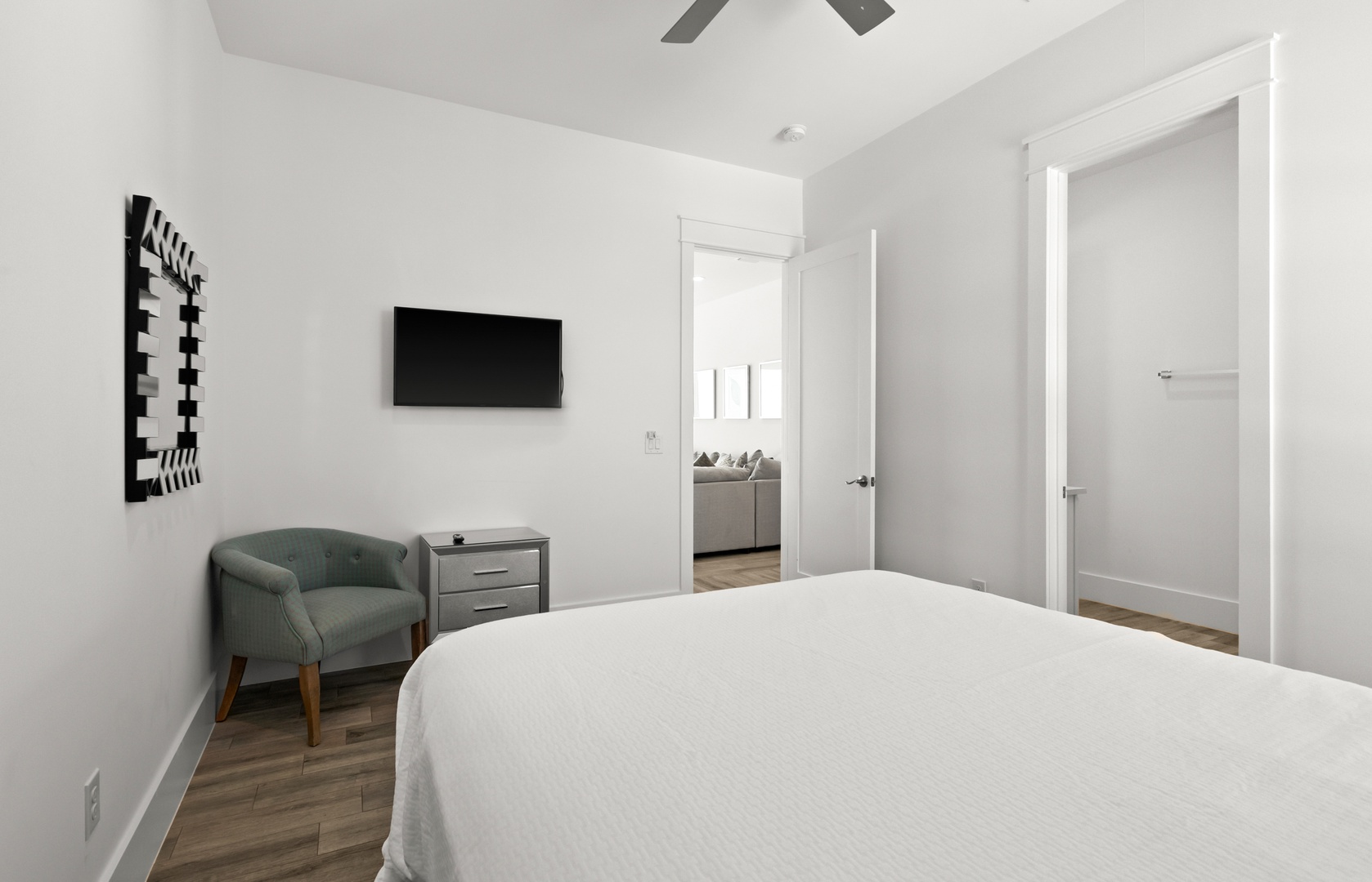 Your serene bedroom retreat features a plush bed, cozy chair, and ceiling fan, all wrapped in modern minimalist style for your perfect night's rest.
