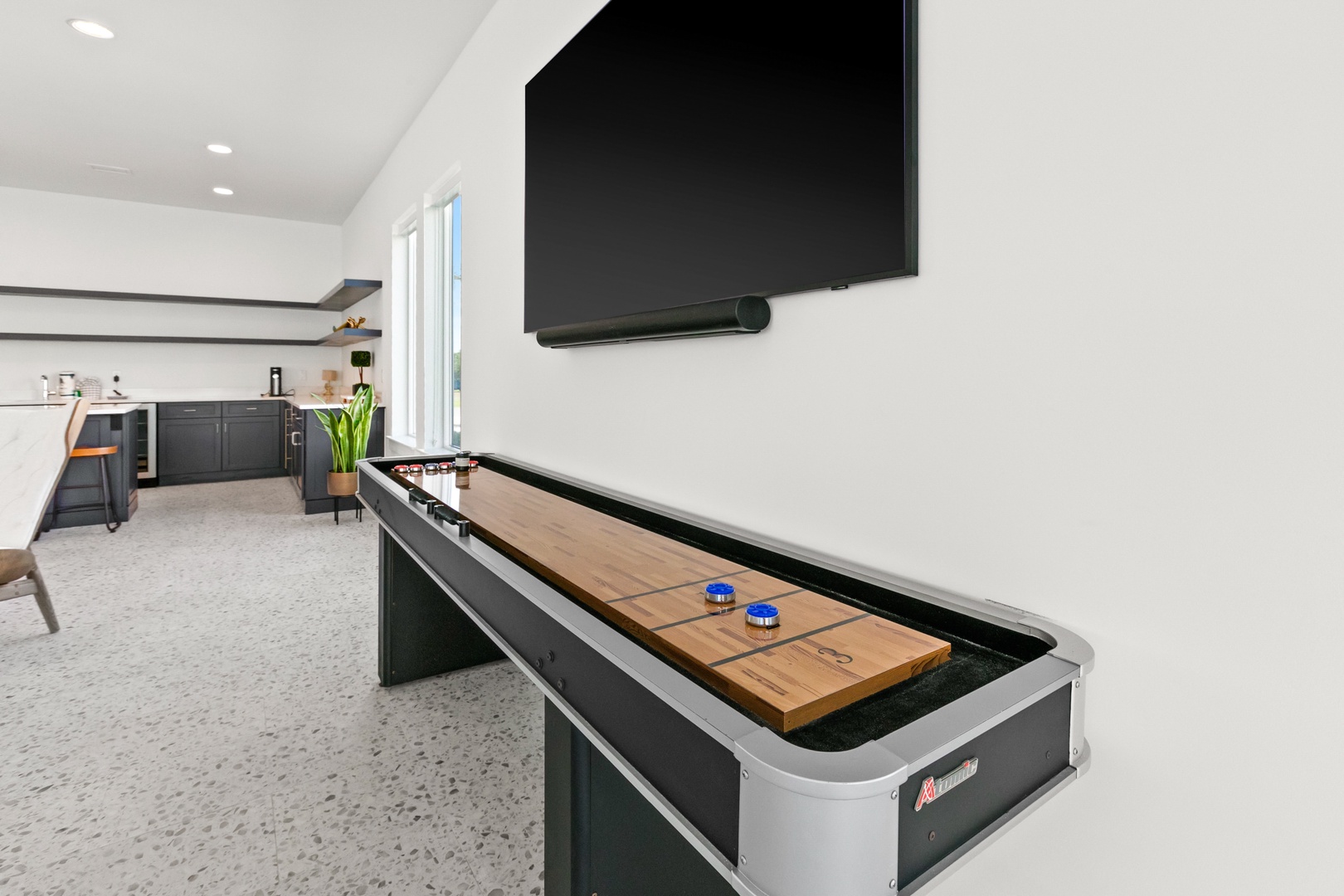 Slide the puck and unwind in your stylish game room, where a sleek shuffleboard table invites friendly competition beneath a bright, modern open-beam ceiling—perfect for cozy evenings in.