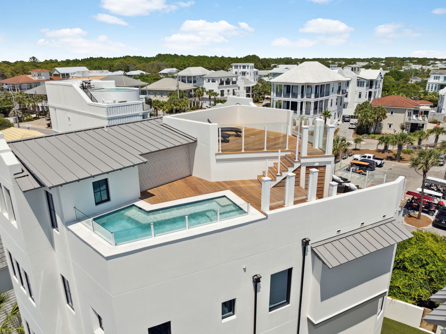 Modern rooftop oasis with private pool, sundeck, and covered lounge space set in a coastal neighborhood with lush landscaping and waterfront homes nearby.