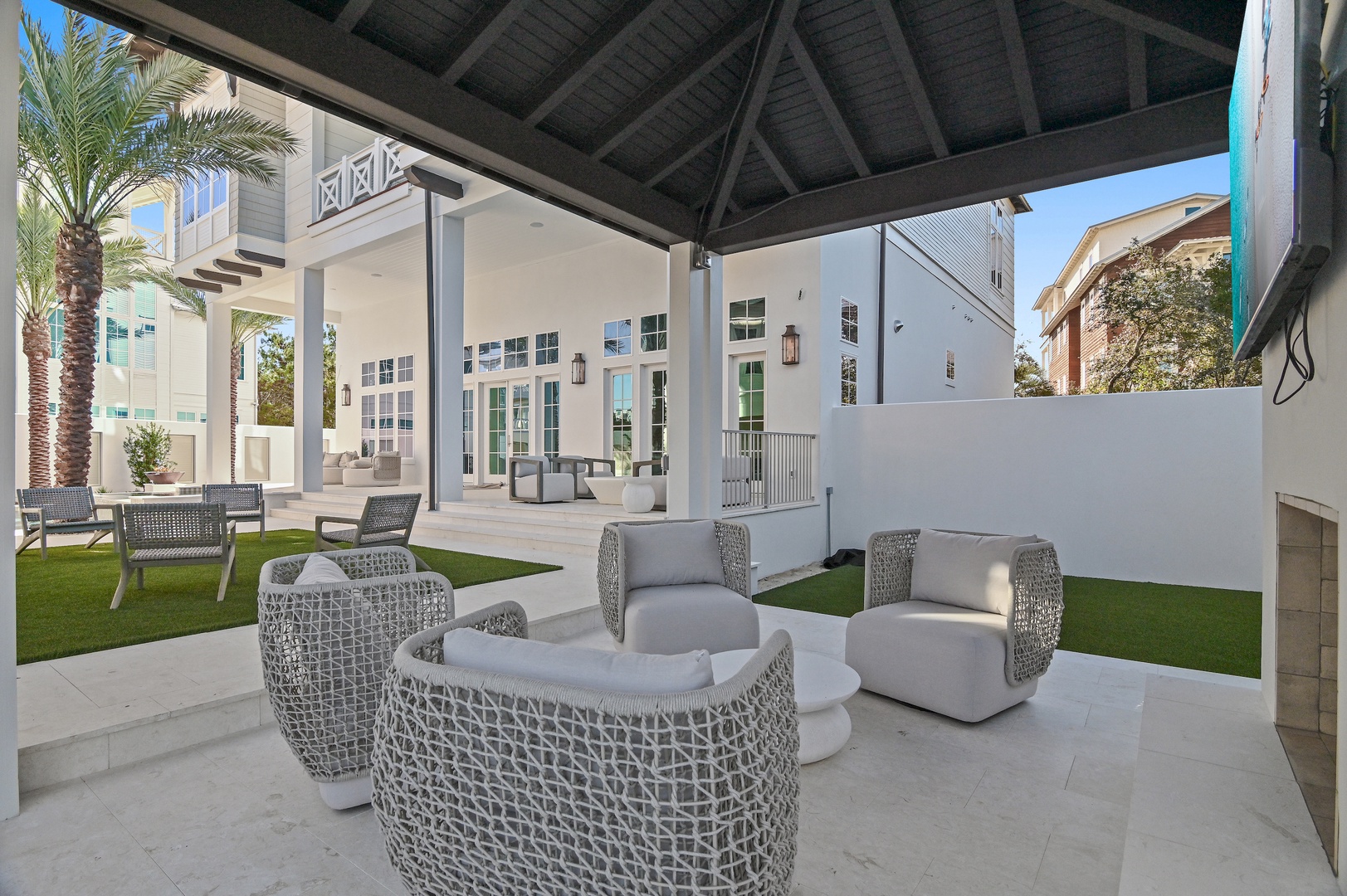 Gather with friends under the covered pavilion, where coastal-chic seating invites you to unwind in the fresh air. Lush greenery and bright skies frame this perfect outdoor retreat.