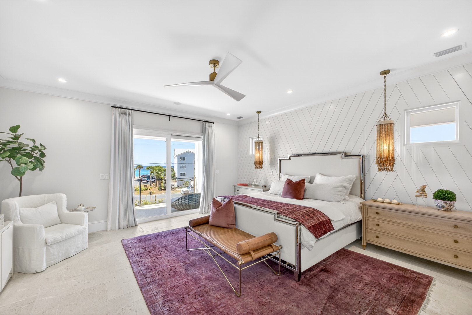 Your elegant bedroom features a plush king bed, coastal views through sliding glass doors, and thoughtful touches like statement pendant lighting and a cozy seating area to unwind after a day at the beach.