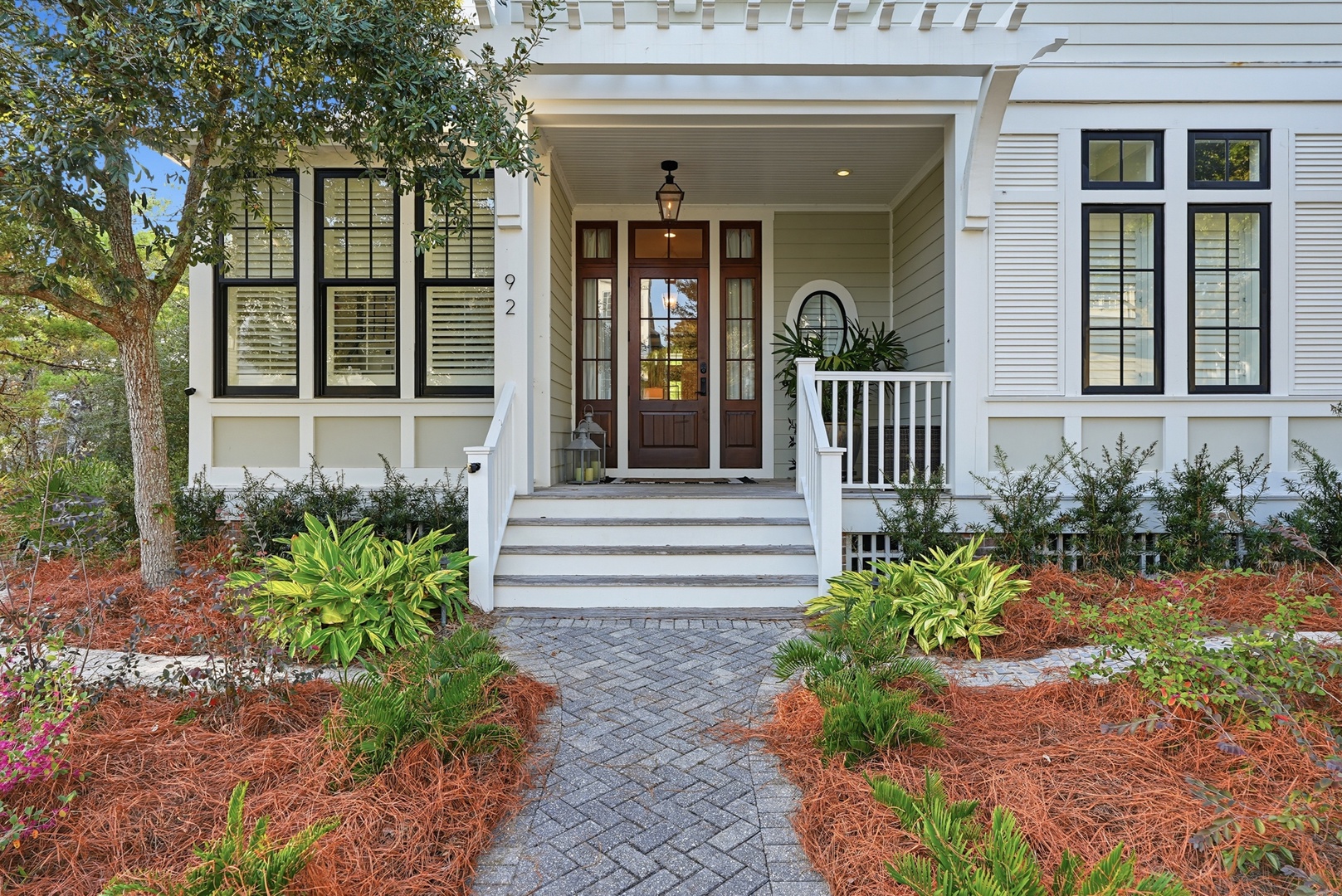 This charming home welcomes guests with a covered front porch, classic white exterior, and lush landscaping that frames the elegant entrance.