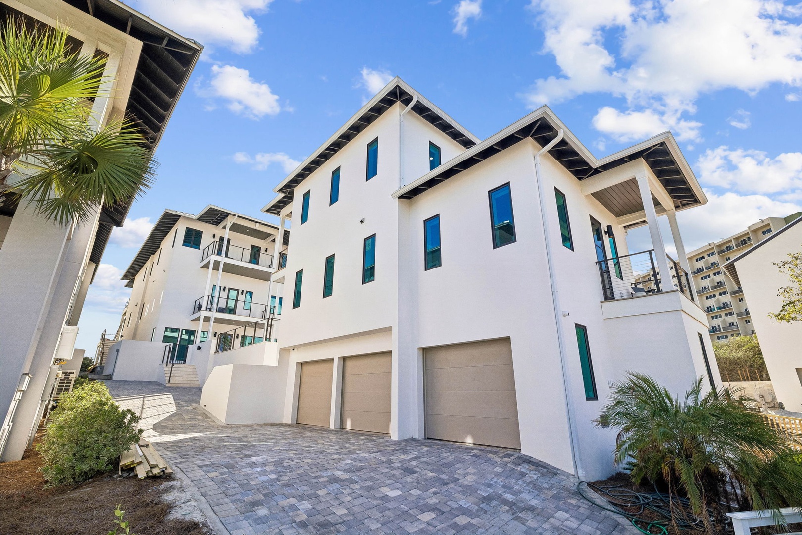 Modern coastal architecture featuring clean white exteriors, spacious balconies, and convenient garage parking in a tranquil beachside neighborhood under blue skies.
