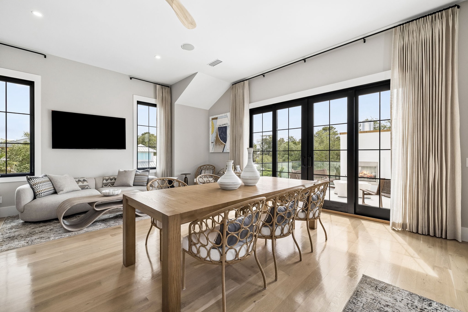 Picture yourself unwinding in this sunlit, open-concept living and dining area where vaulted ceilings and large windows frame serene views, inviting you to relax and gather around the warm wood table.