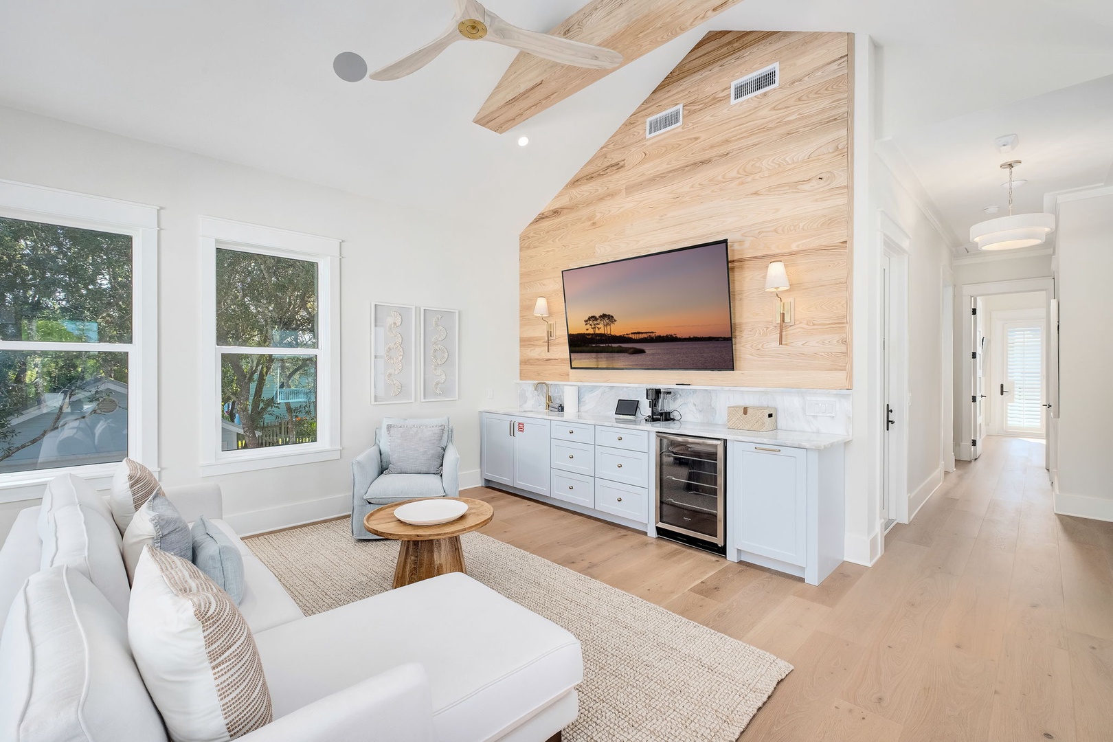 Relax in this bright living room where natural light floods in through large windows. A cozy seating area with plush sofas and a warm wood accent wall creates your perfect spot to unwind after exploring the area.