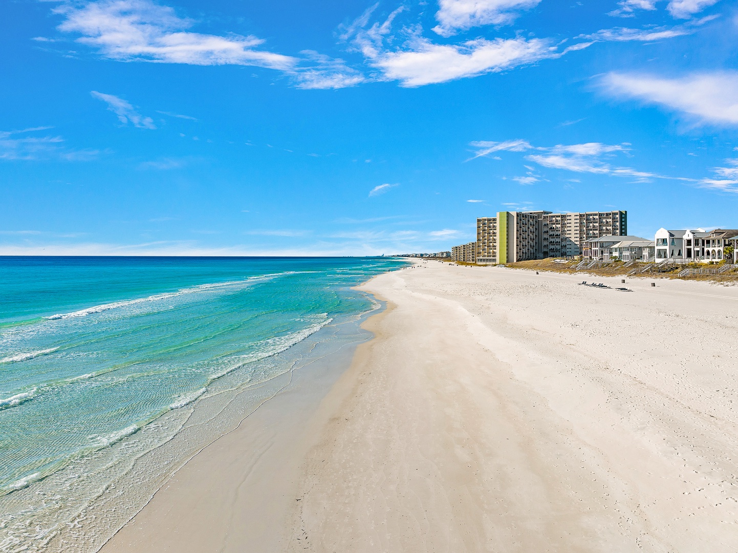 Pristine white sand beach stretches along turquoise waters with beachfront accommodations and clear blue skies overhead.