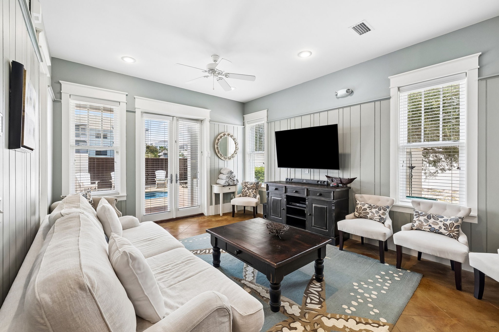 Relax in your bright, coastal-inspired living room with comfy seating, charming shiplap walls, and direct access to the pool through French doors—perfect for laid-back afternoons.