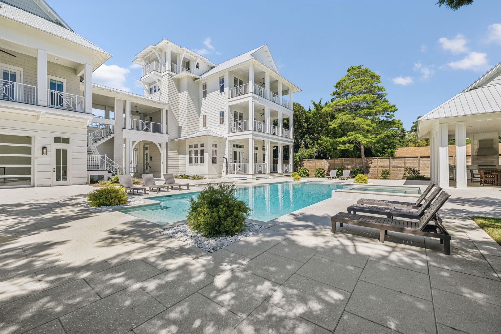 An elegant multi-story vacation home featuring a pristine swimming pool surrounded by manicured landscaping and modern architecture with classic coastal design.