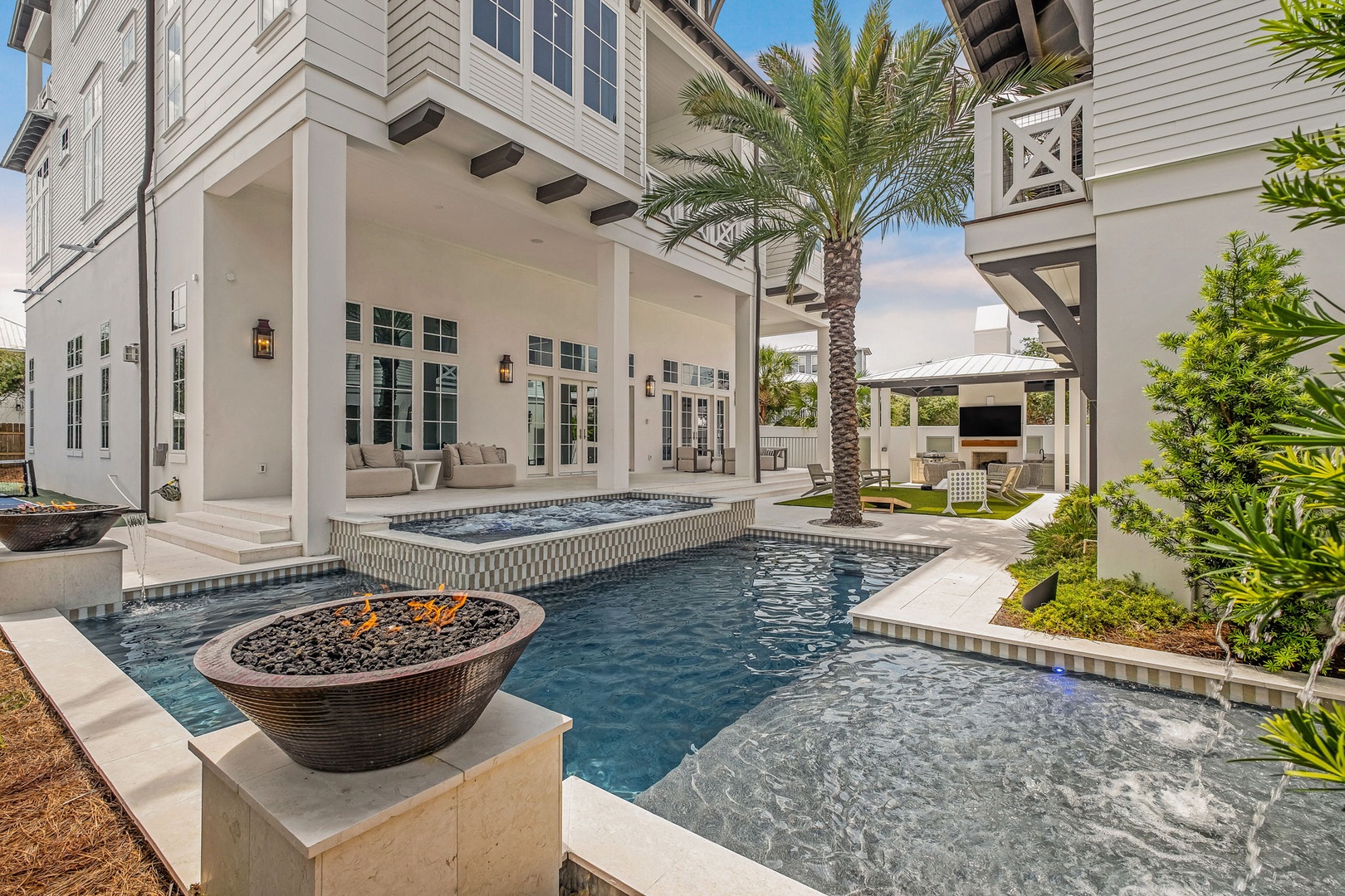 A stunning outdoor paradise awaits with a sparkling pool, integrated hot tub, and cozy fire feature—your perfect spot to unwind under swaying palms and sunny skies.