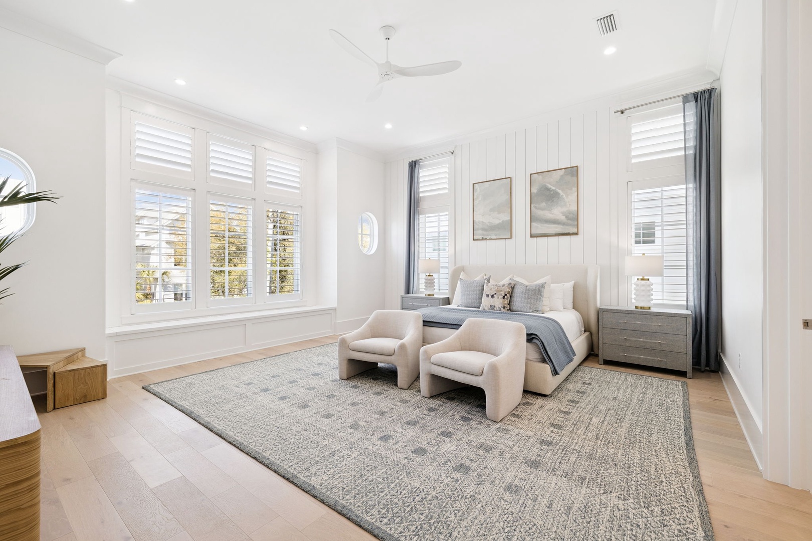 Sink into your luxurious king bed surrounded by elegant white paneling and plush seating, where natural light filters through plantation shutters.