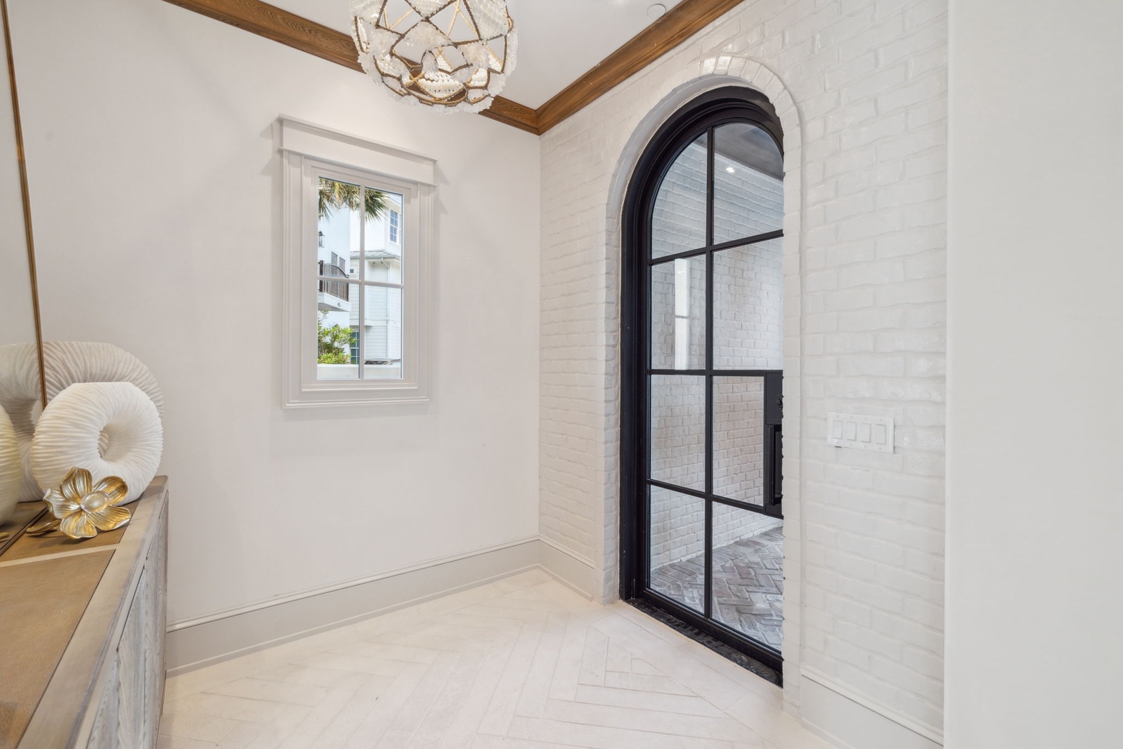 Step into this bright, elegant entryway where architectural details and natural light create an inviting first impression. The stunning arched glass door and warm wood beams set the stage for your coastal retreat.