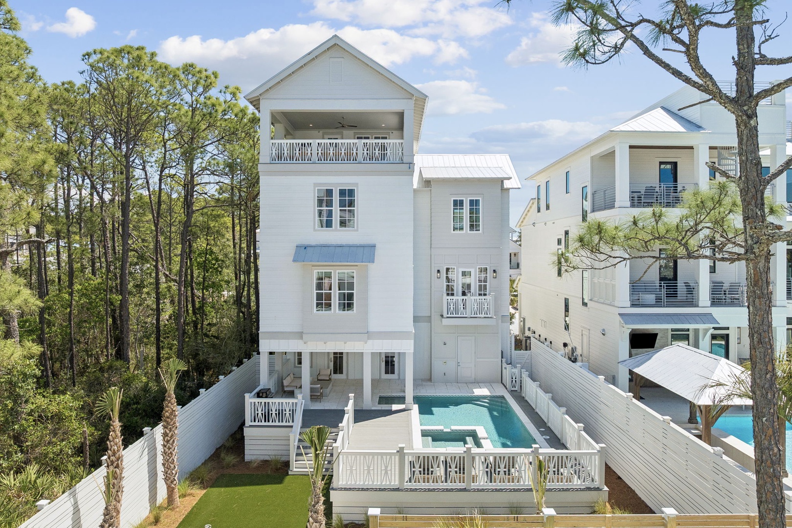Modern coastal home with private pool nestled among towering pines, featuring clean white architecture and multiple outdoor living spaces.