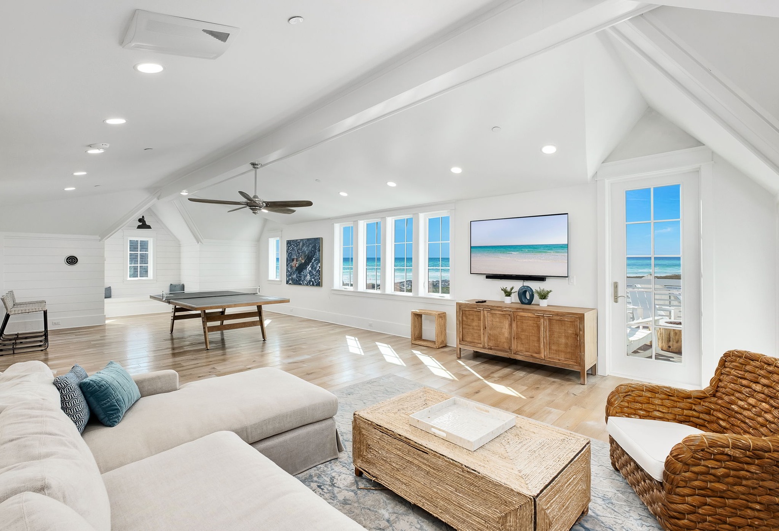 Relax in this bright, coastal living space with soaring vaulted ceilings, natural wood furnishings, and stunning ocean views through floor-to-ceiling windows.
