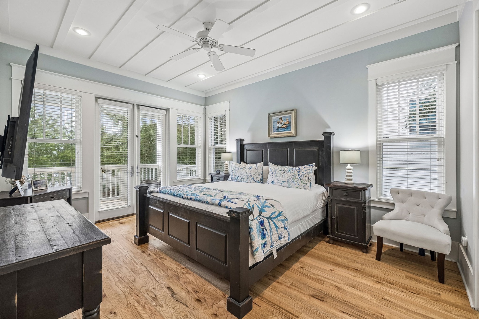 Step into your serene coastal retreat, where soft morning light spills through French doors onto gleaming hardwood. Coastal-inspired linens dress the plush bed, while a reading chair invites quiet moments before you step outside.