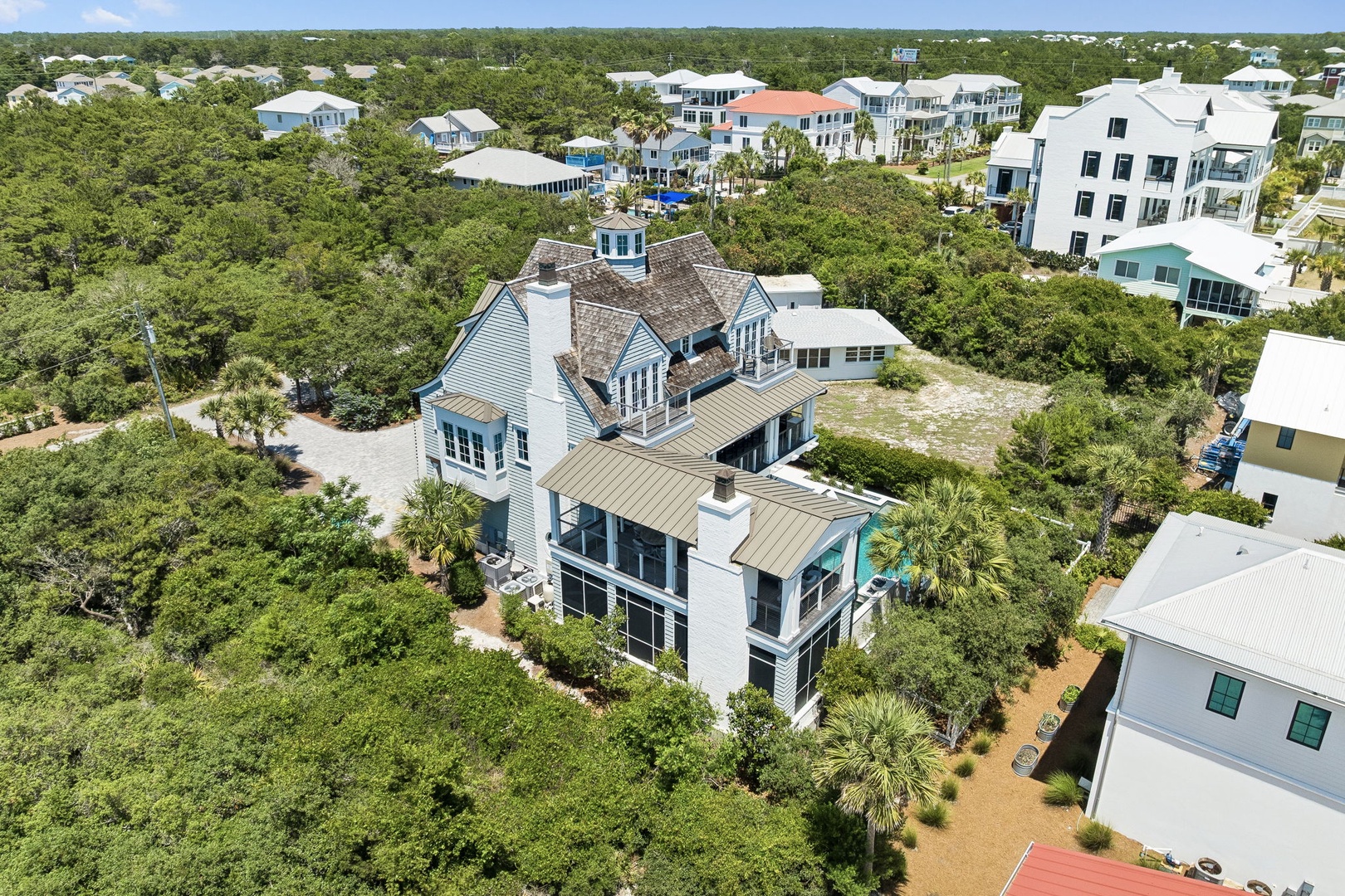 Aerial view of a distinctive coastal property nestled among native vegetation and palm trees in a quiet residential neighborhood, showcasing the surrounding natural landscape and nearby homes.
