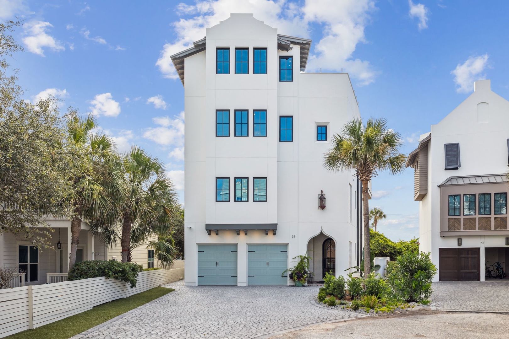 A striking coastal rental with tropical palms, turquoise accents, and paver driveway—capturing the sunny, relaxed vibe of a beachside neighborhood.