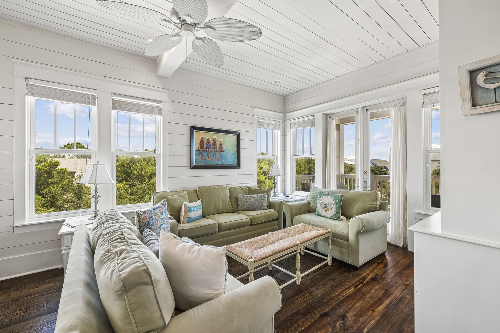 You'll love unwinding in this bright, coastal living room where shiplap walls and a ceiling fan create a breezy, relaxed feel. Large windows frame the lush natural landscape and fill the space with daylight.