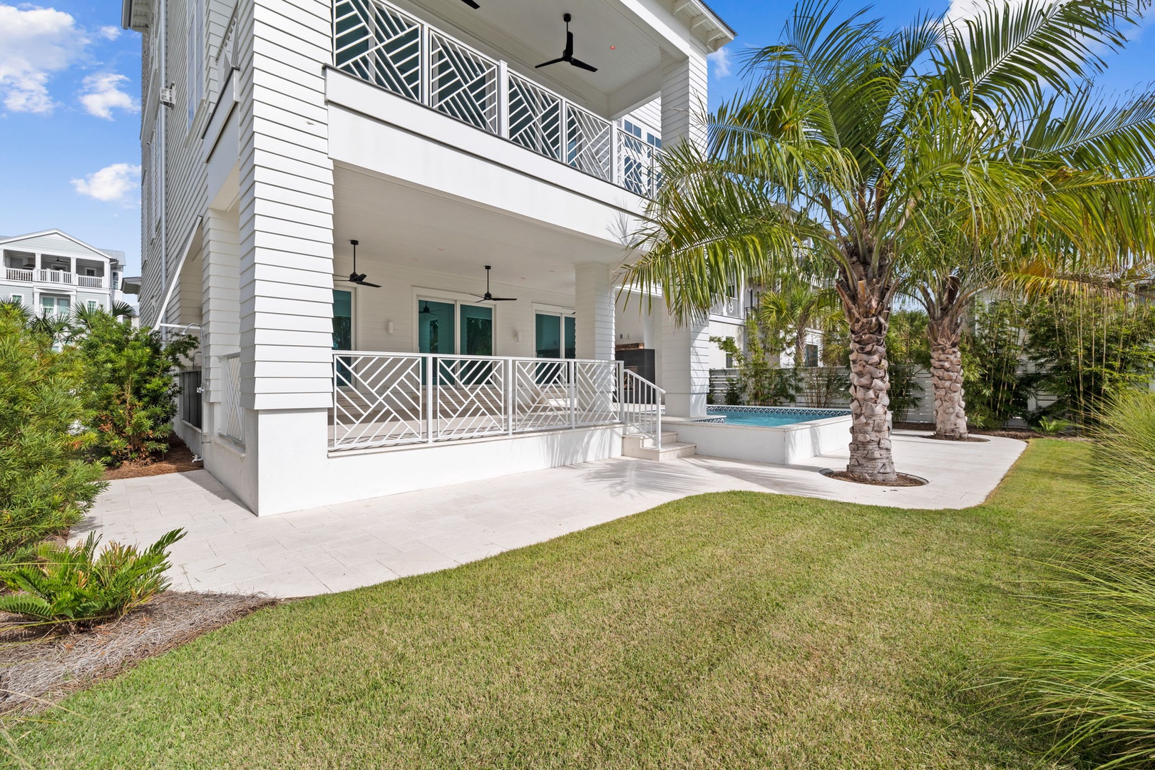 Modern coastal property featuring tropical landscaping with palm trees, pristine lawn, and elegant white architecture with decorative balcony railings.
