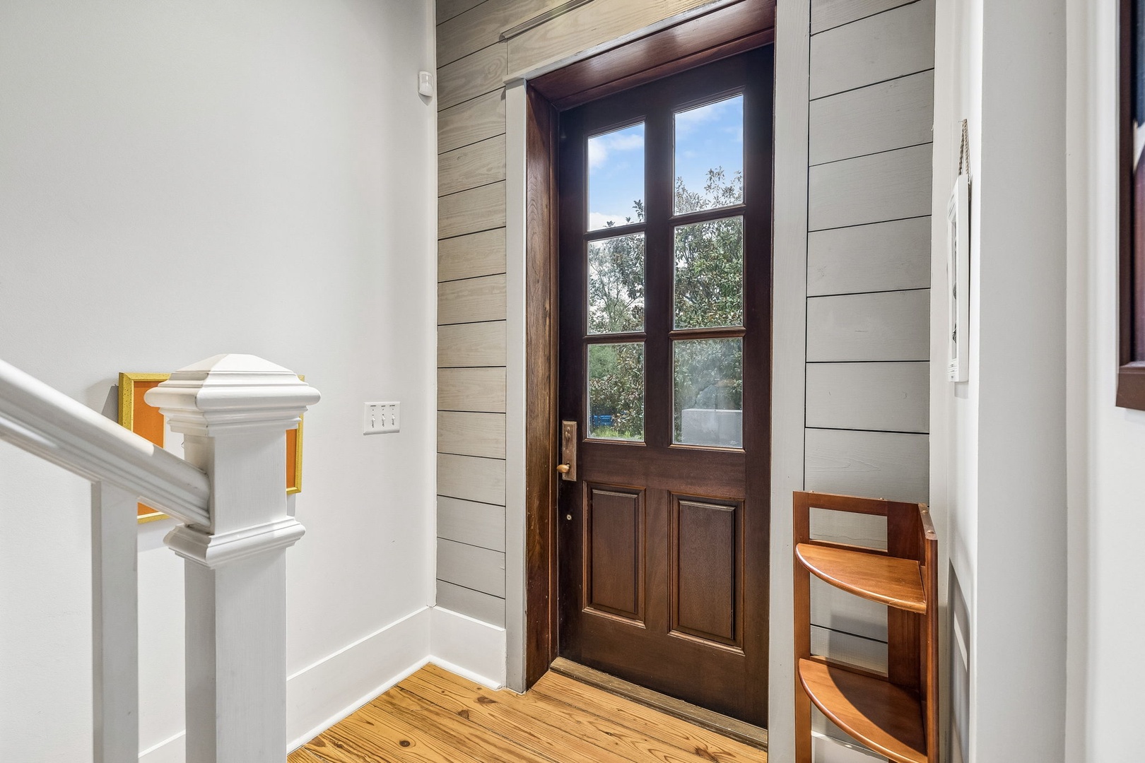 A welcoming entryway with charming shiplap and rich hardwood floors invites you into your home-away-from-home, where peaceful greenery and blue skies greet you through classic French doors.