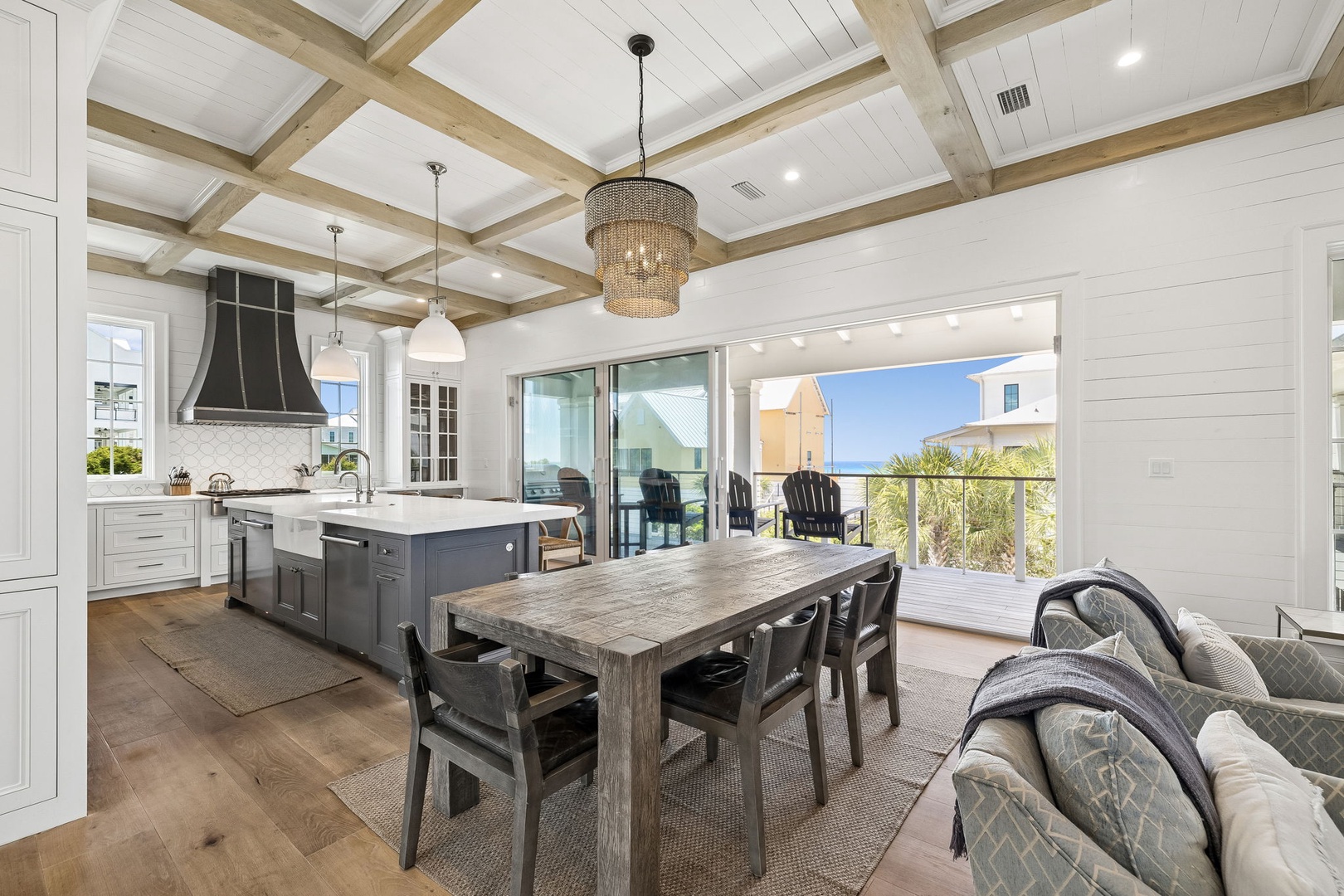 You'll love gathering around this beautifully crafted dining table with coffered ceiling above and coastal views beyond. The open kitchen makes hosting effortless while you soak in the natural light streaming through.
