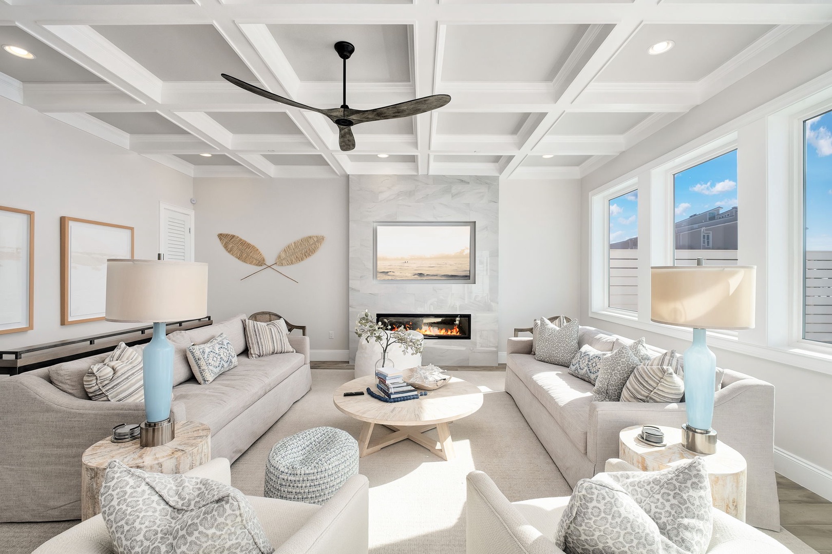 Sink into plush seating beneath soaring coffered ceilings where natural light floods through oversized windows, creating your perfect coastal retreat.