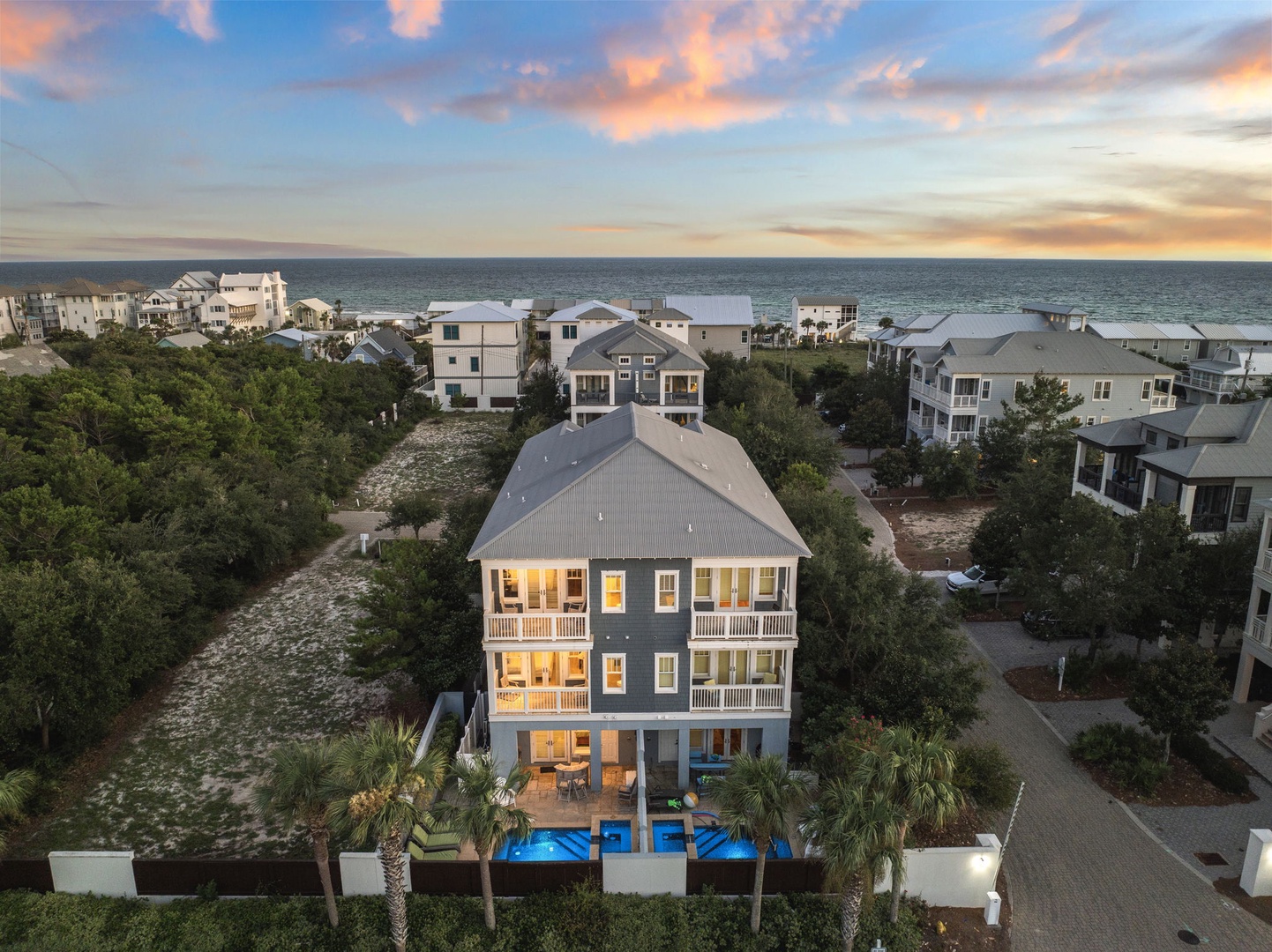 This stunning coastal property showcases classic beach architecture with sweeping ocean views, nestled among lush greenery just steps from the shore. The private pool and multiple balconies capture breathtaking sunsets over the Gulf.